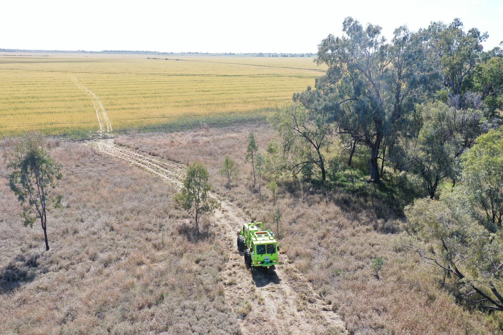 Aerial view of a green seismic survey vehicle on a rural access track through Australian bushland and cropland