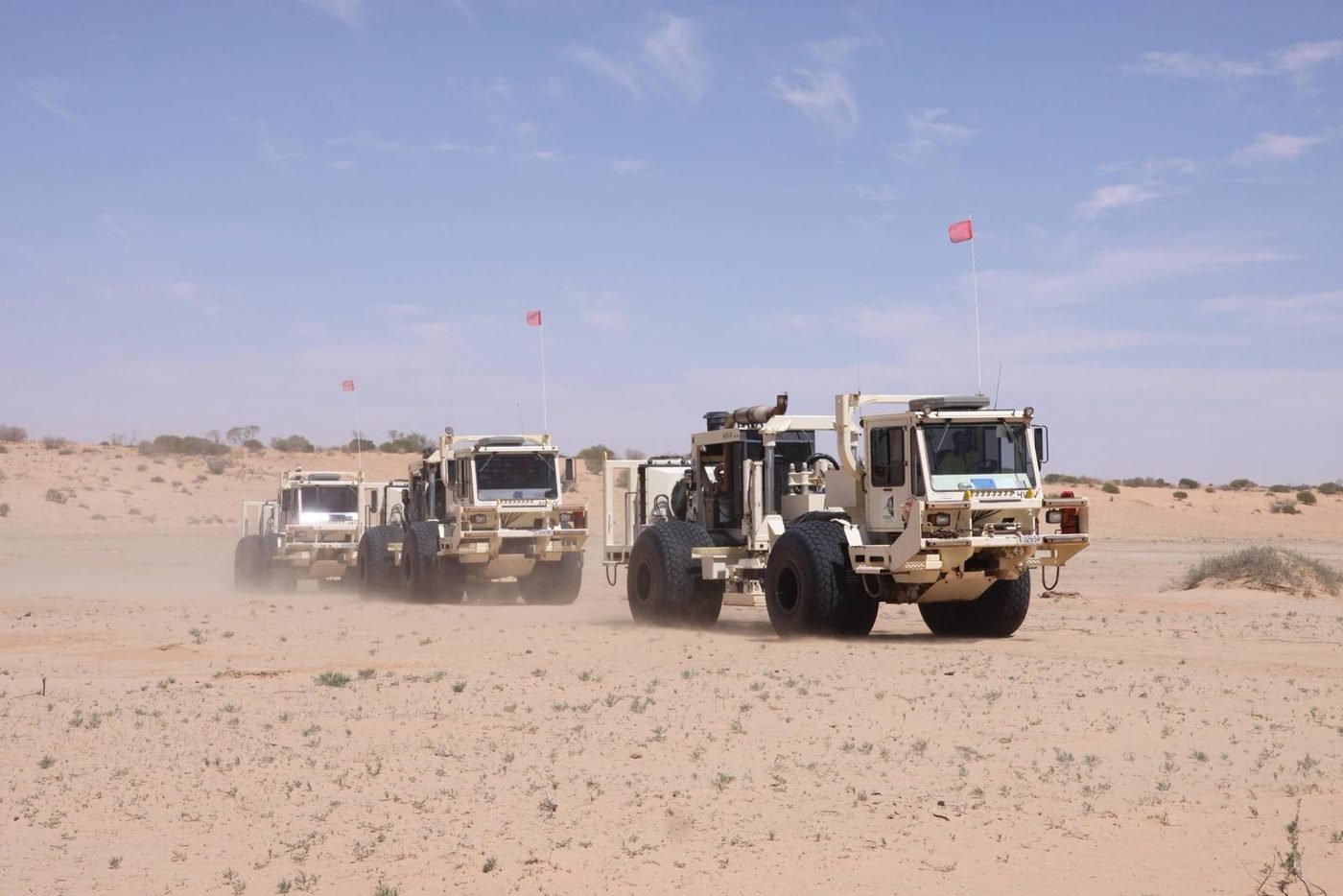 Convoy of vibroseis units raising dust in desert terrain, Cooper Basin, South Australia