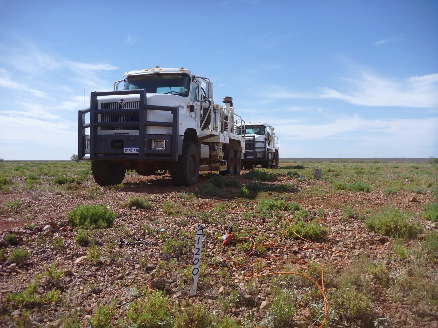 White vibroseis survey trucks with a seismic point marker in the field, Eromanga Basin, Queensland